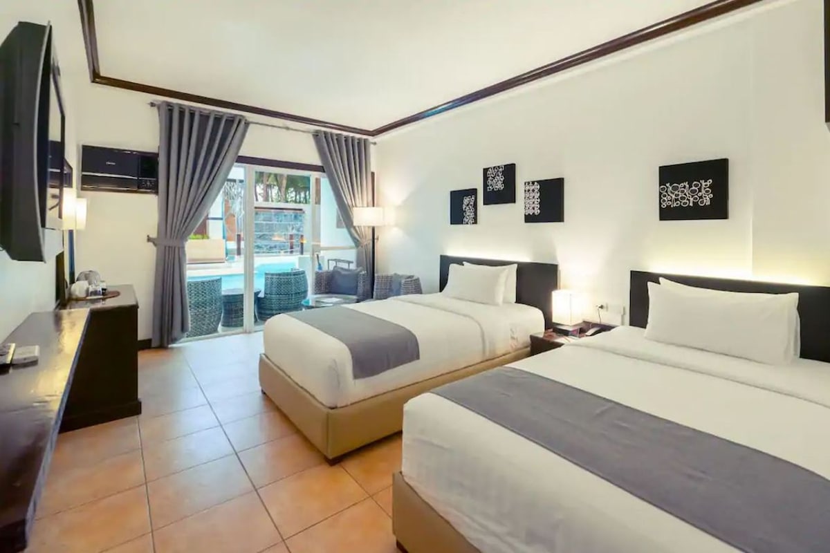 Habitación de hotel con dos camas, un escritorio, un televisor y un balcón con cortinas.
