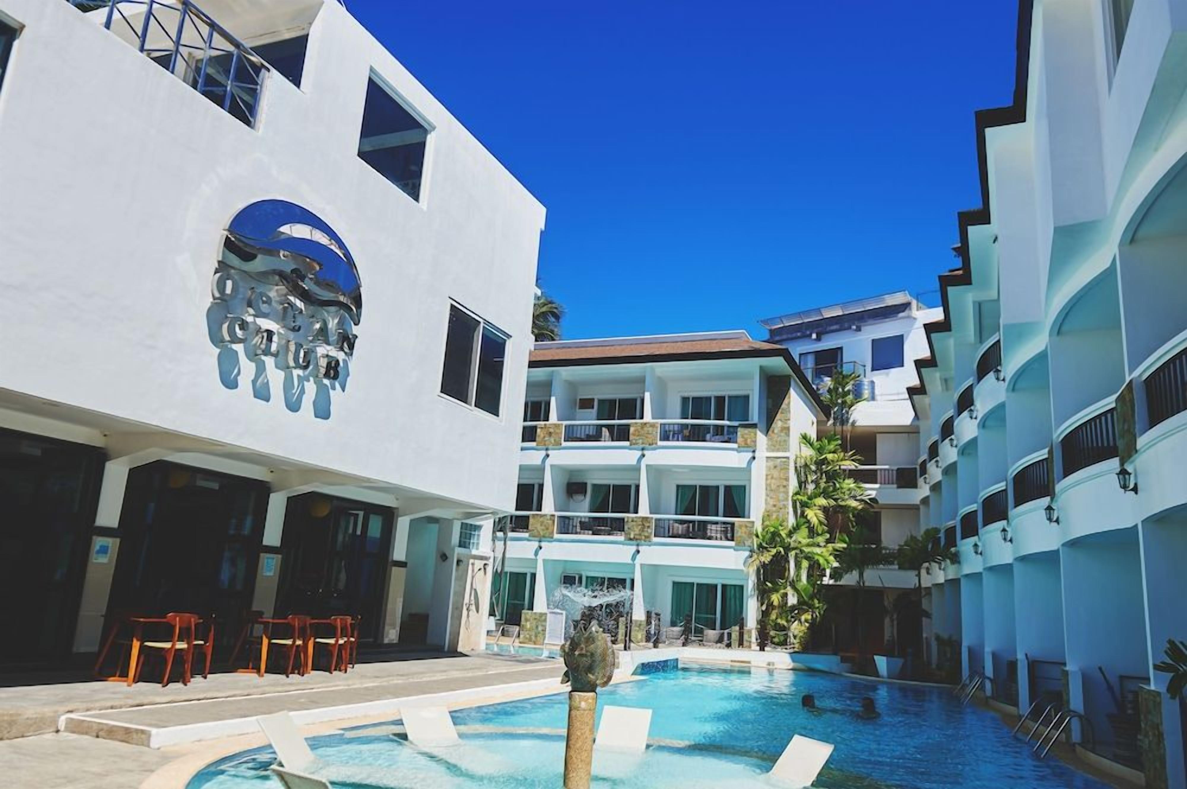 A hotel with a pool area, outdoor seating, and a clear blue sky.