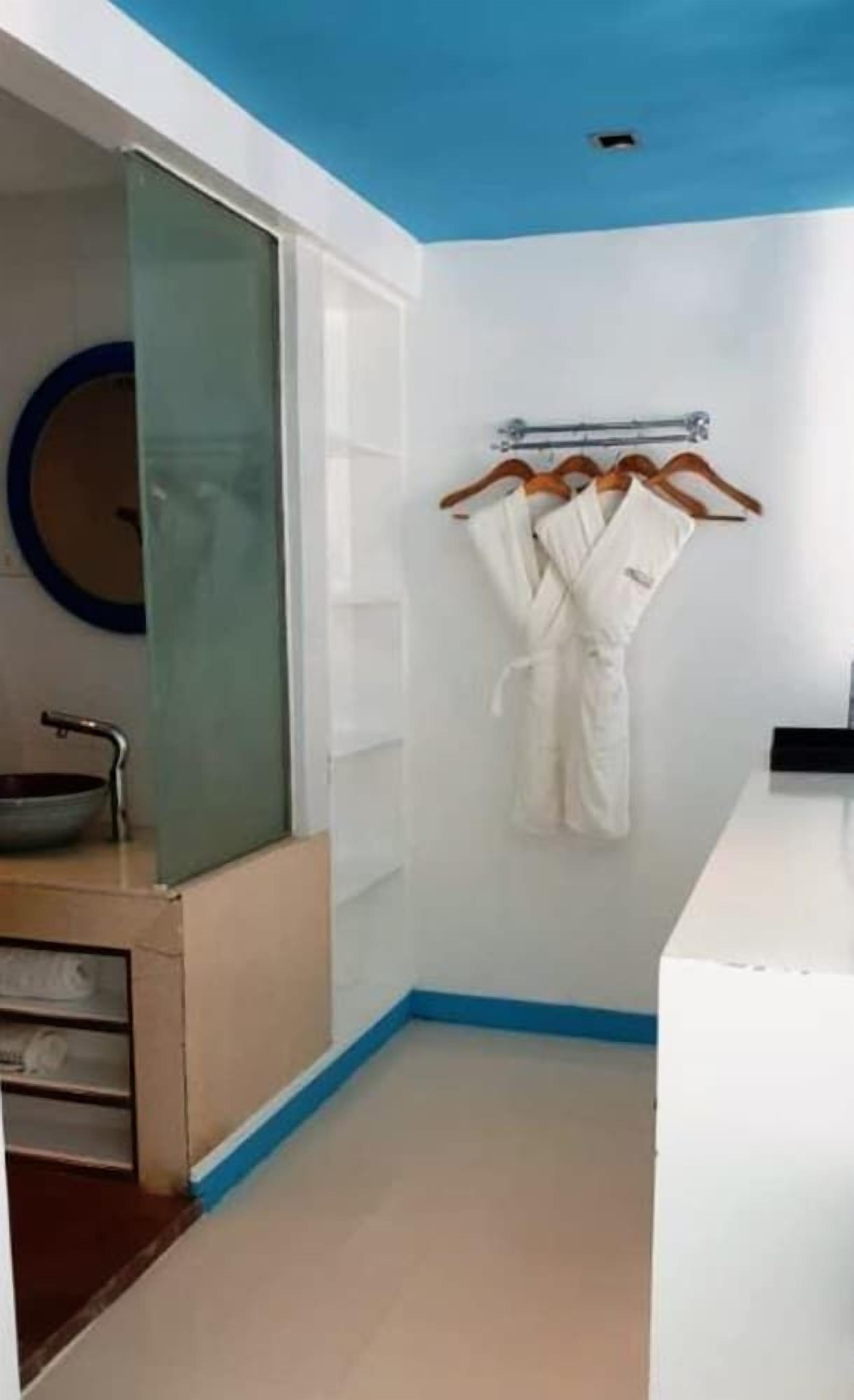 Un baño moderno con cabina de ducha de vidrio, un lavabo blanco y un perchero con batas.