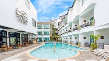 Un patio de hotel con piscina, mobiliario exterior y varios balcones.