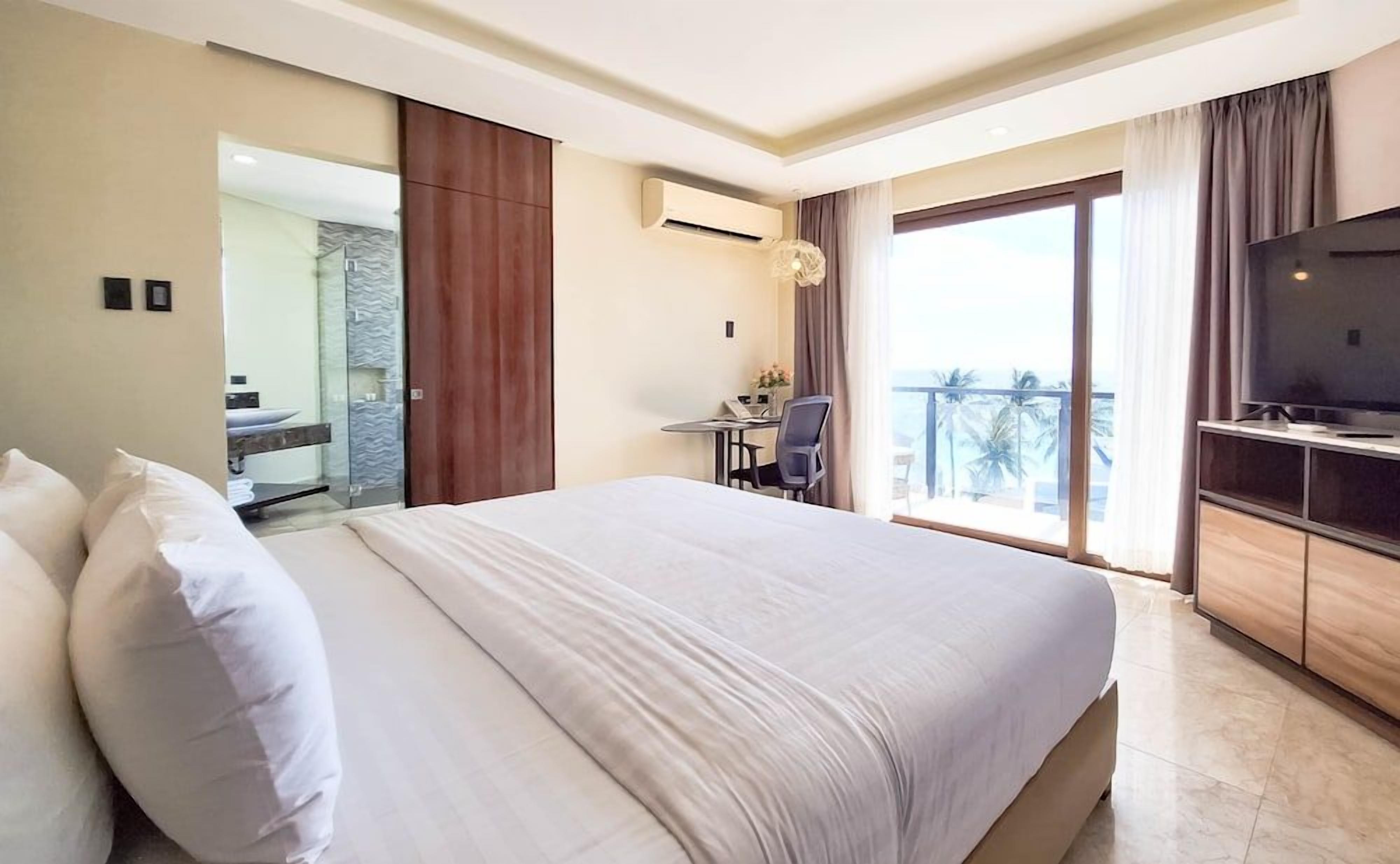 Habitación de hotel con una cama grande, un escritorio con silla, televisión y balcón con vistas.