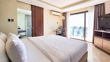 Habitación de hotel con una cama grande, un escritorio con silla, televisión y balcón con vistas.
