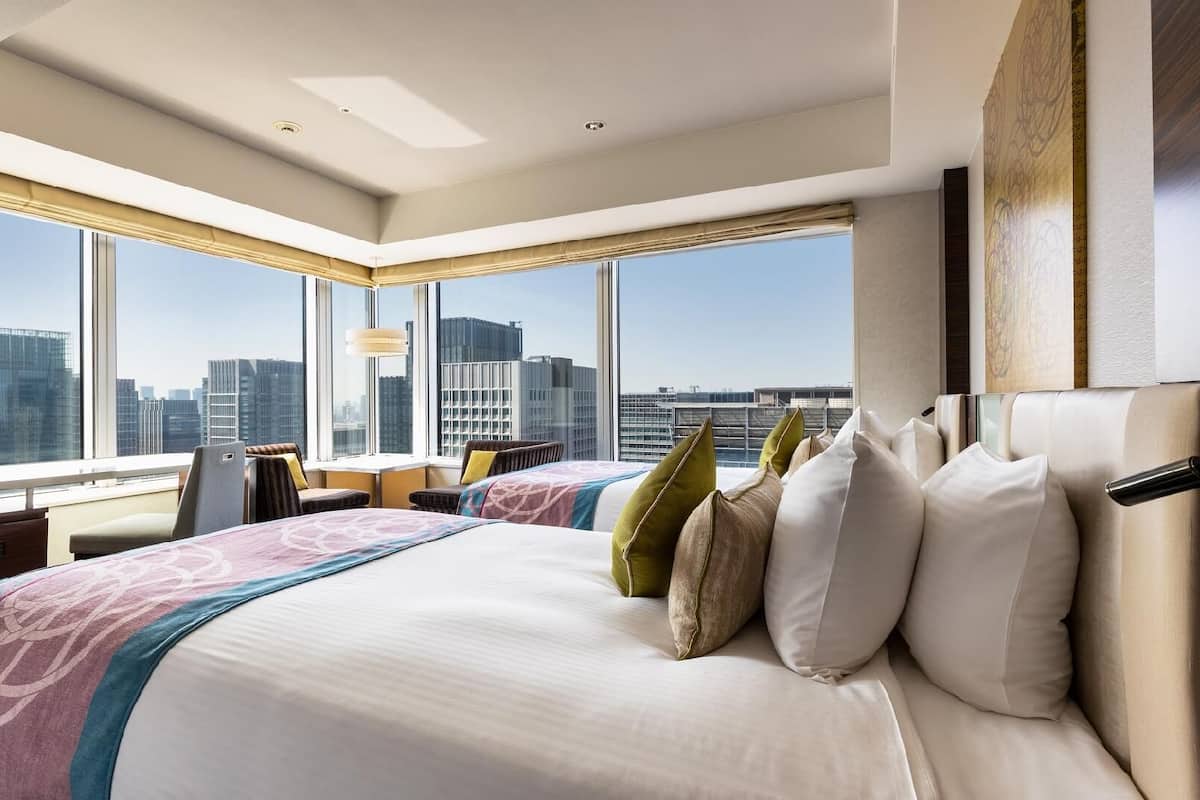 A hotel room with a large bed, two chairs, a desk, and a view of the cityscape.