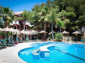 A pool area with lounge chairs and umbrellas, surrounded by palm trees and a building with a red facade.