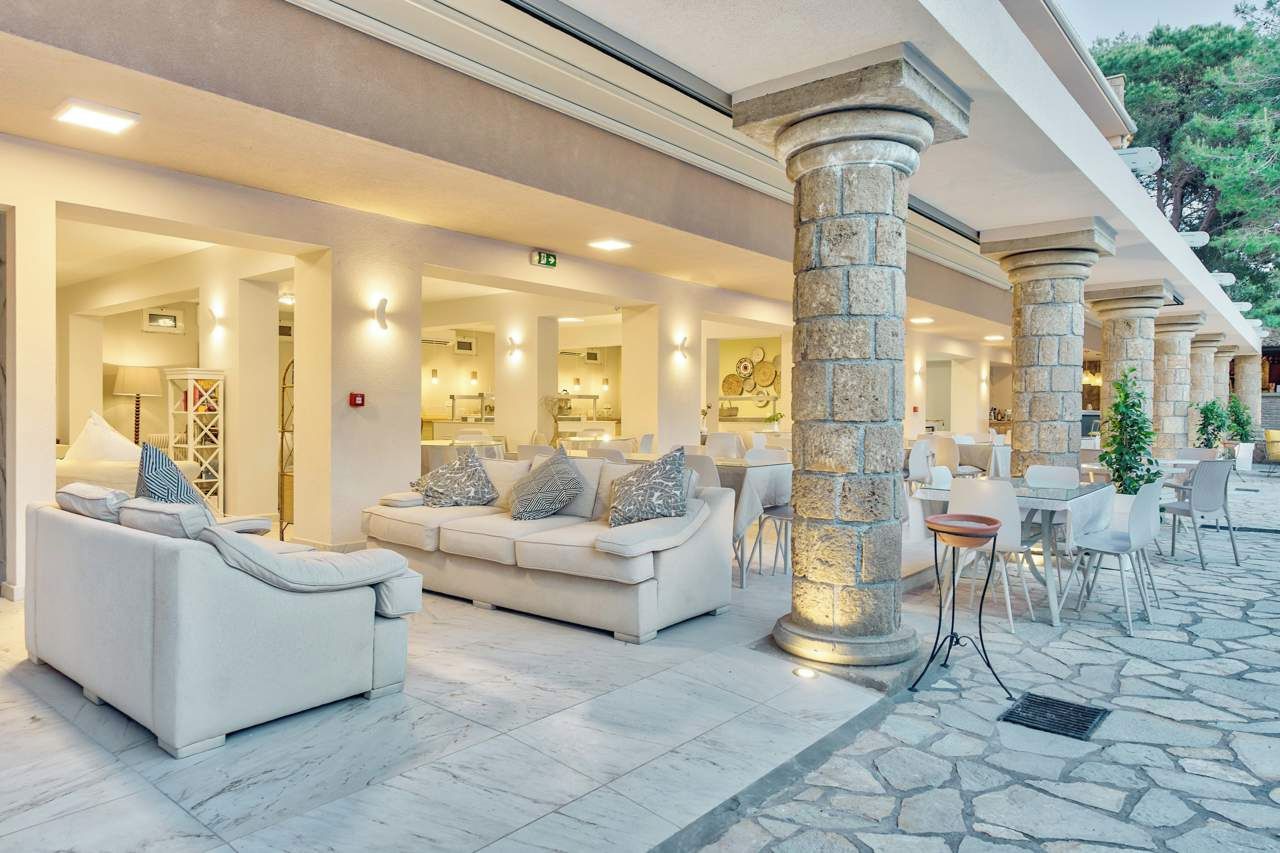 A hotel lobby with a white sofa, a stone column, and a dining area with tables and chairs.