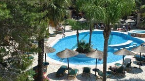 Zona de piscina con sillas de descanso, sombrillas y palmeras.