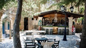 Un patio al aire libre con suelo de piedra, mesas y sillas de madera, una barra con mostrador de piedra y faroles colgantes.