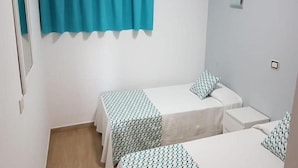 A small, clean room with two single beds, a window with a blue curtain, and a white wall.