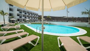 A pool area with sun loungers and umbrellas, surrounded by a building with balconies.