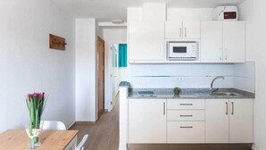 A modern kitchen with white cabinets, a microwave, and a sink. There is a dining table with chairs and a vase of flowers. - Montesol Atsol (Mogan)