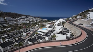 A coastal residential area with modern white buildings, a curved road, and a clear view of the sea.