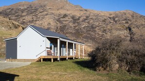 A small cabin with a porch, set against a mountainous backdrop. - Shotover Country Cottages (Lower Shotover)