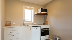 A compact kitchen with a built-in dishwasher, oven, and microwave shelf. - Shotover Country Cottages (Lower Shotover)