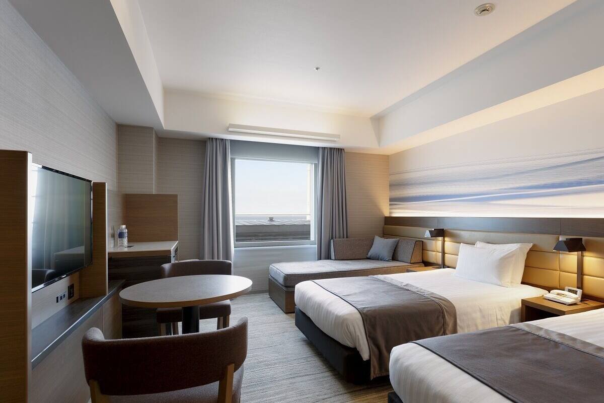 Une chambre d’hôtel avec un lit, un bureau, une chaise, une télévision et une grande fenêtre.
