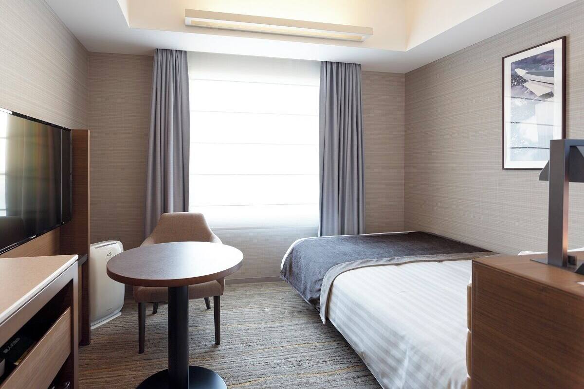 Une chambre d’hôtel avec un lit, un bureau, une chaise, une télévision et une fenêtre avec des rideaux.