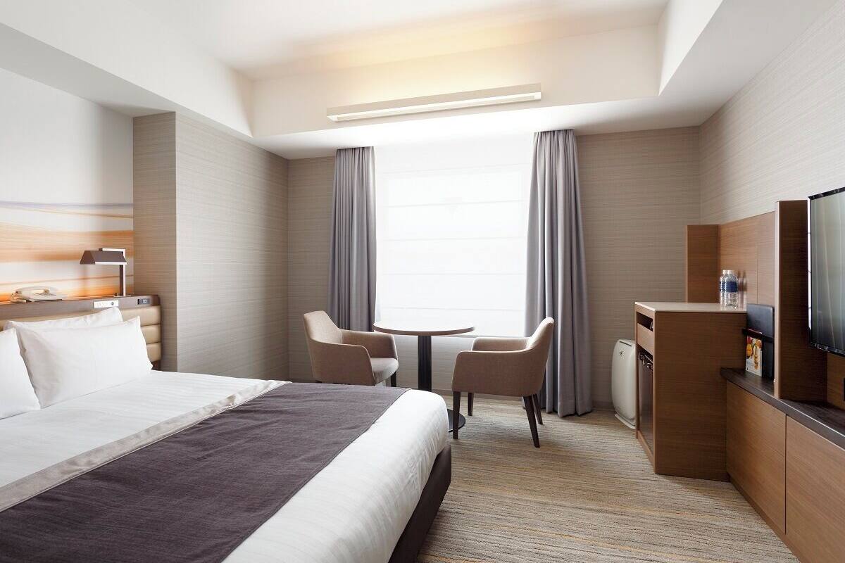 Une chambre d’hôtel équipée d’un lit, d’un bureau, d’une chaise, d’une télévision et d’une fenêtre avec des rideaux.