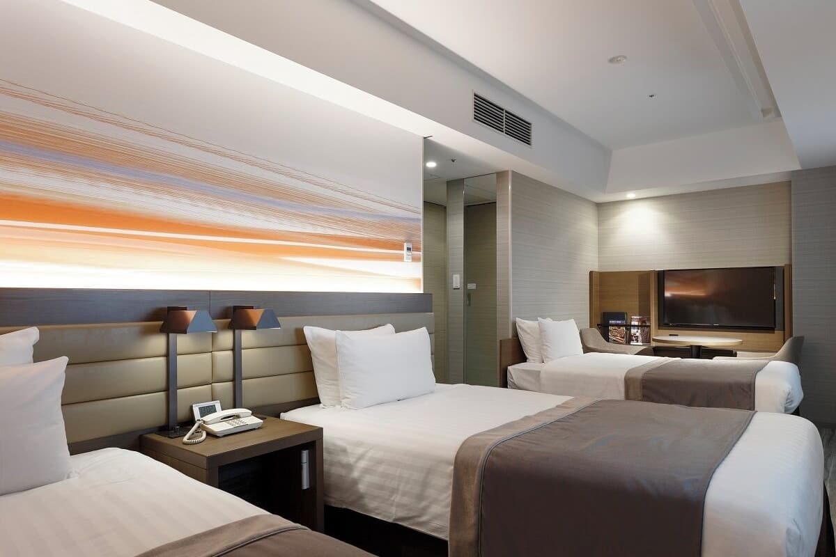 Une chambre d’hôtel avec deux lits, une télévision, un bureau avec un téléphone et une télévision fixée au mur.