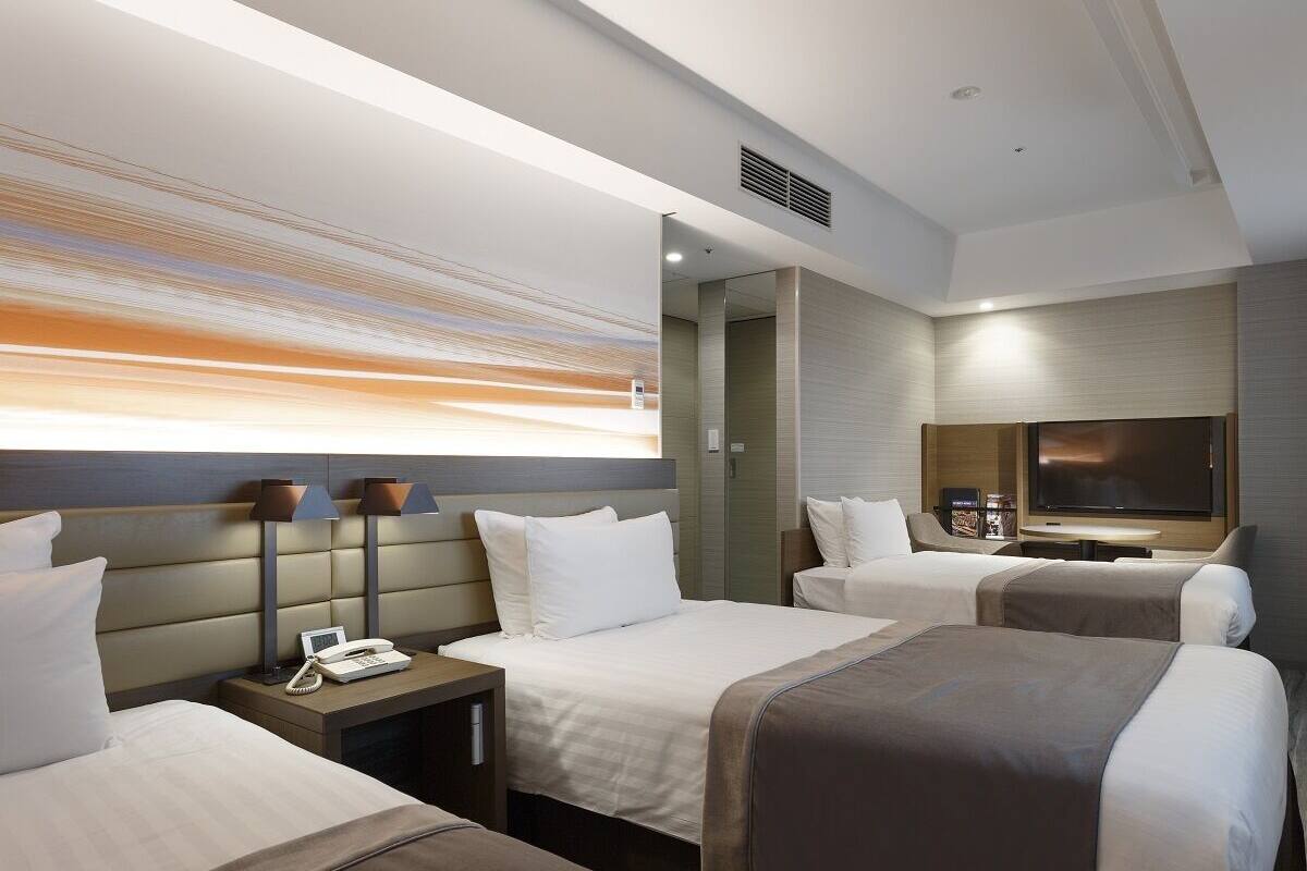 Une chambre d’hôtel avec deux lits, une télévision, un bureau avec un téléphone et une télévision fixée au mur.
