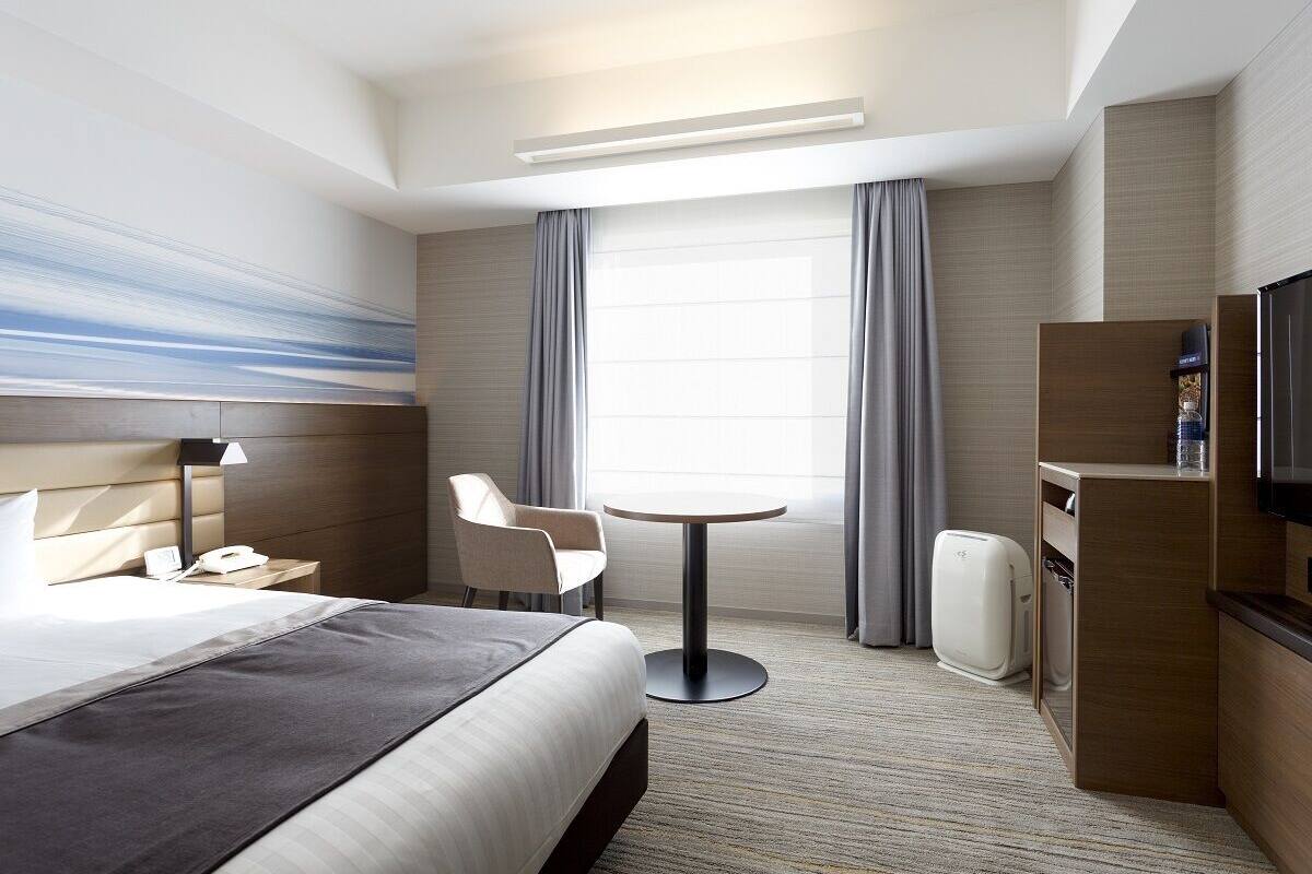 Une chambre d’hôtel avec un lit, une table ronde, une chaise, un téléviseur et un mini-bar.