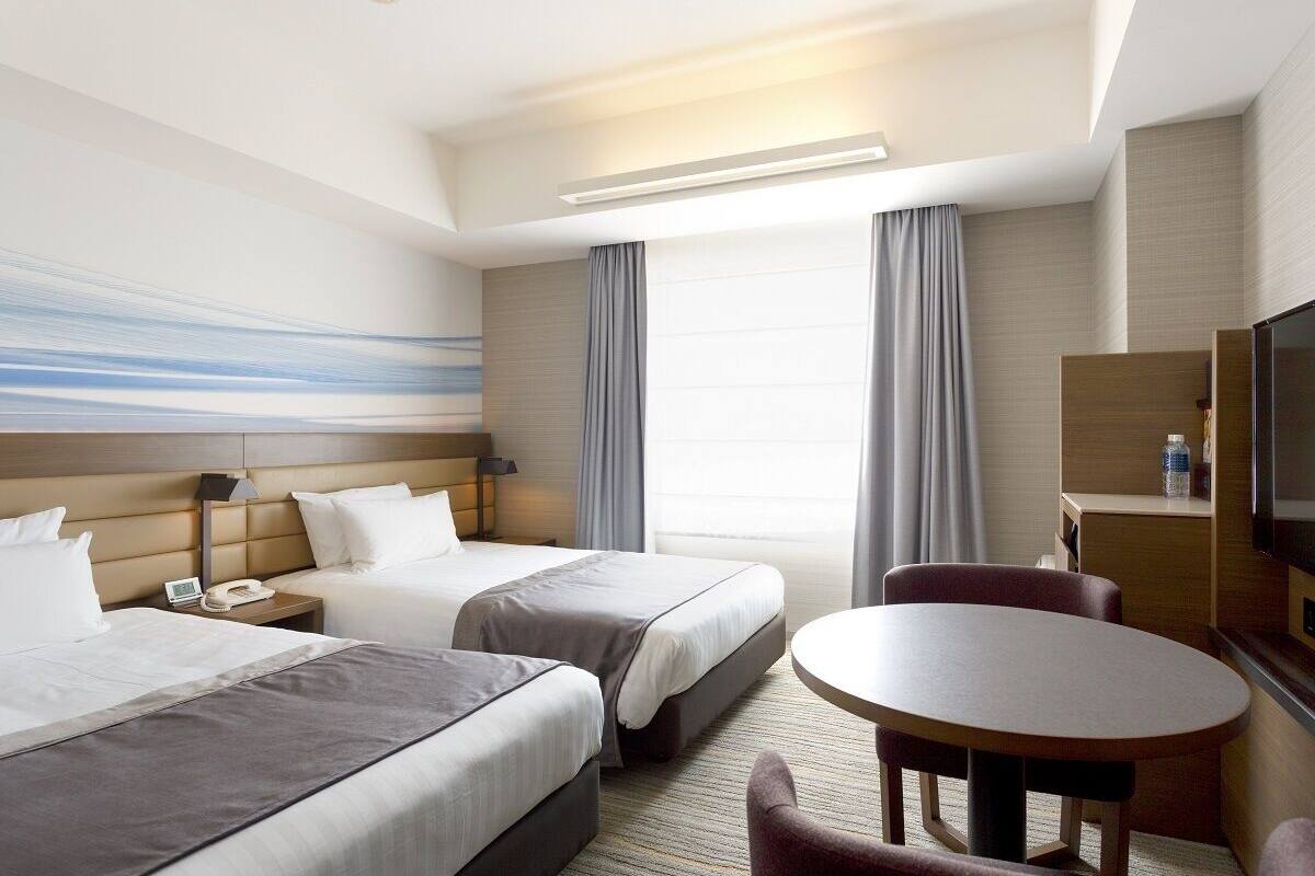 Une chambre d’hôtel avec deux lits, un bureau, une chaise, une t élévision et une grande fenêtre avec des rideaux.
