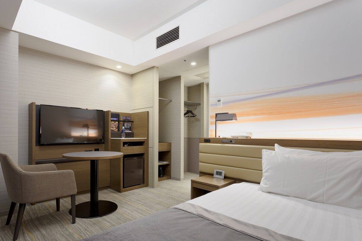 Une chambre d’hôtel comprenant un lit, un bureau avec une chaise, une télévision, un minibar et un espace douche.