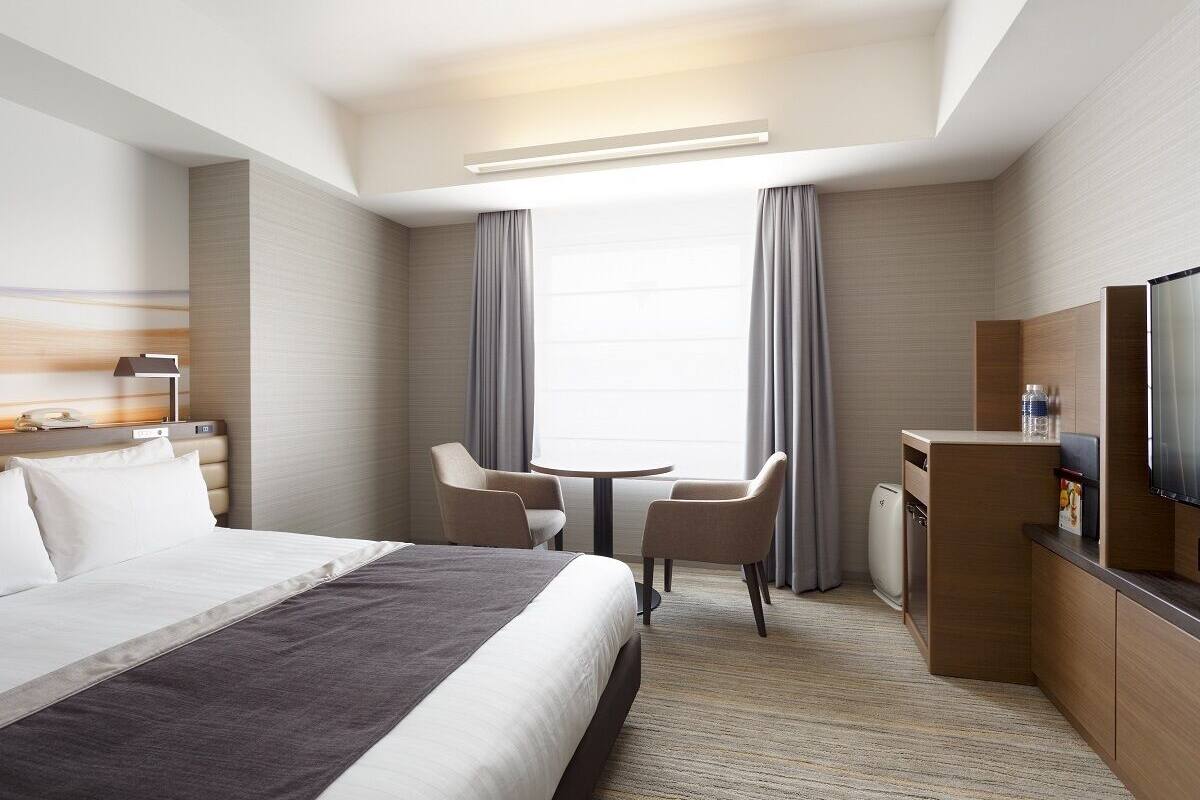 Une chambre d’hôtel équipée d’un lit, d’un bureau, d’une chaise, d’une télévision et d’une fenêtre avec des rideaux.