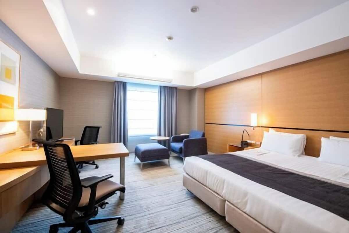 Une chambre d’hôtel équipée d’un lit, d’un bureau, d’un fauteuil de bureau et d’un petit coin salon.