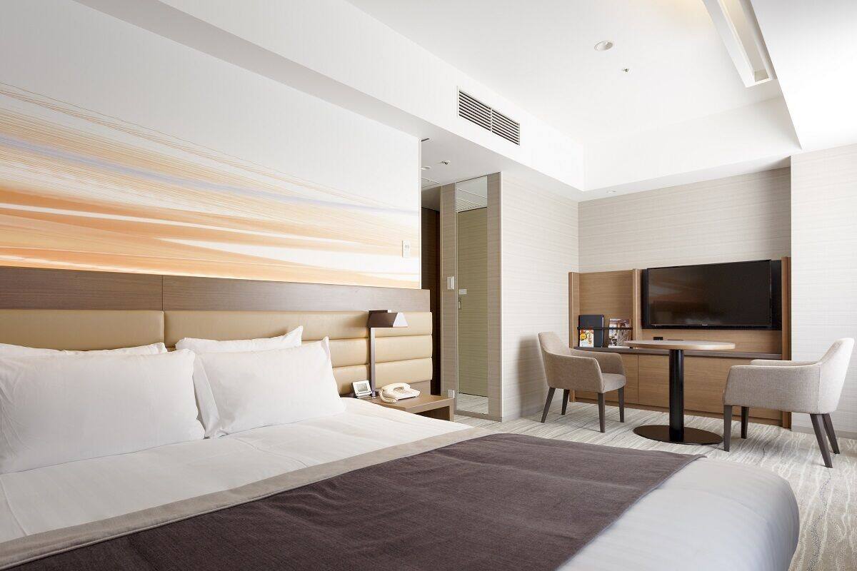 Une chambre d’hôtel avec un grand lit, un bureau avec une télévision et une chaise.
