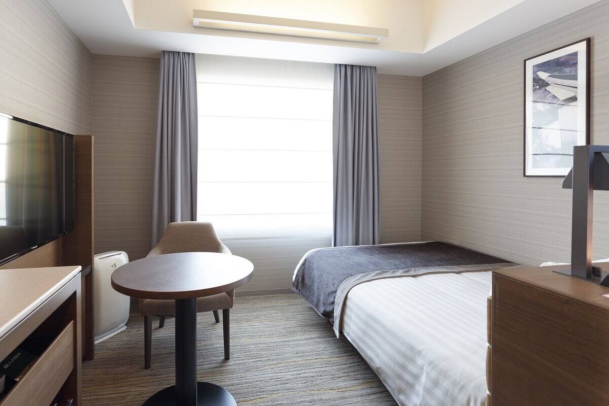 Une chambre d’hôtel équipée d’un lit, d’un bureau, d’une chaise, d’une télévision et d’une grande fenêtre avec des rideaux.