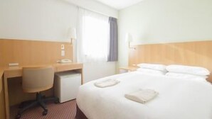 Ein Hotelzimmer mit Bett, Schreibtisch, Stuhl, Telefon und einem Fenster mit Vorhängen.