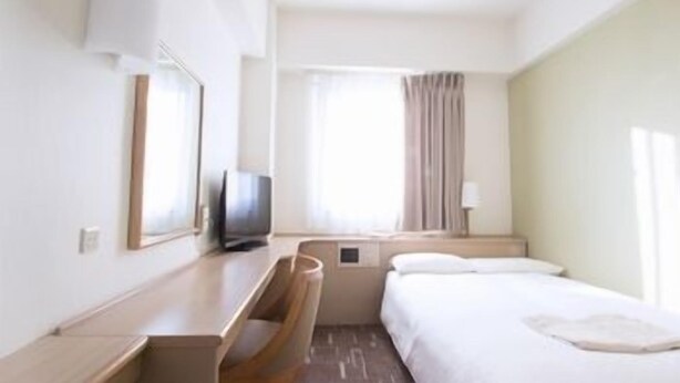 Ein Hotelzimmer mit Bett, Schreibtisch, Fernseher und einem fenster mit Vorhängen.