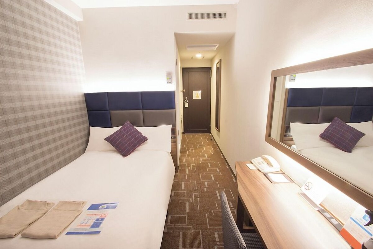 A hotel room with two beds, a desk with a telephone, and a mirror.
