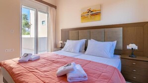A hotel room with a large bed, a wooden headboard, a painting on the wall, and a balcony with curtains. - Selini Villas (Platanias)