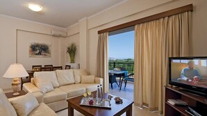 A living room with a sofa, a coffee table, a TV, and a balcony with curtains. - Selini Villas (Platanias)