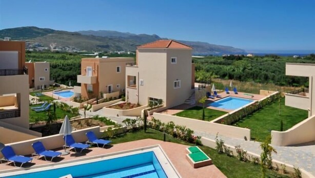 A resort with multiple buildings, outdoor swimming pools, and a view of the sea and mountains. - Selini Villas (Platanias)