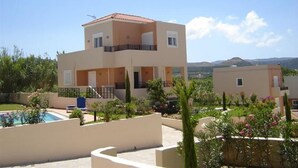 A two-story building with a swimming pool, surrounded by greenery and a clear sky. - Selini Villas (Platanias)