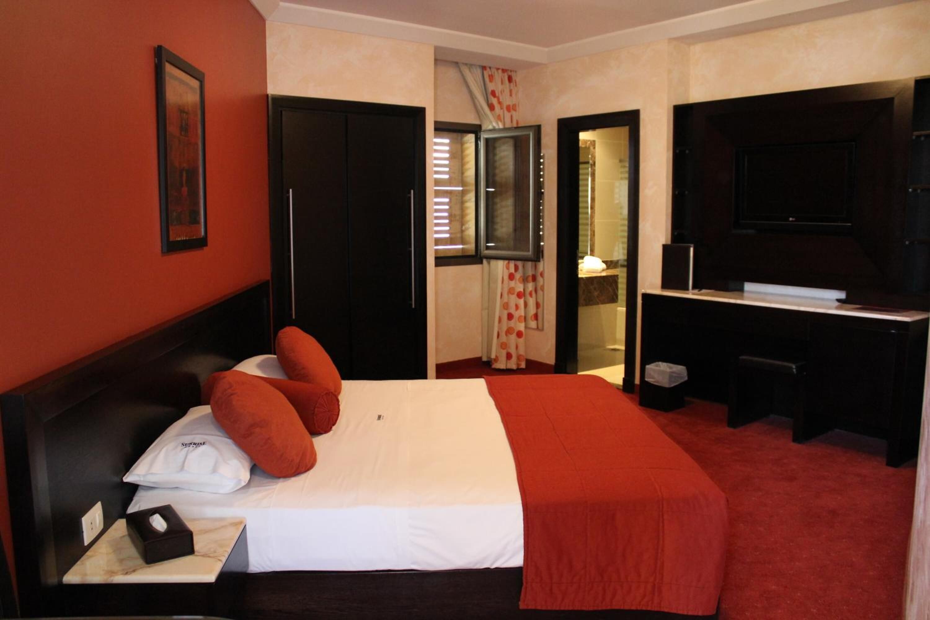Habitación de hotel con una cama grande, un escritorio, una televisión y un baño visible a través de una puerta abierta.