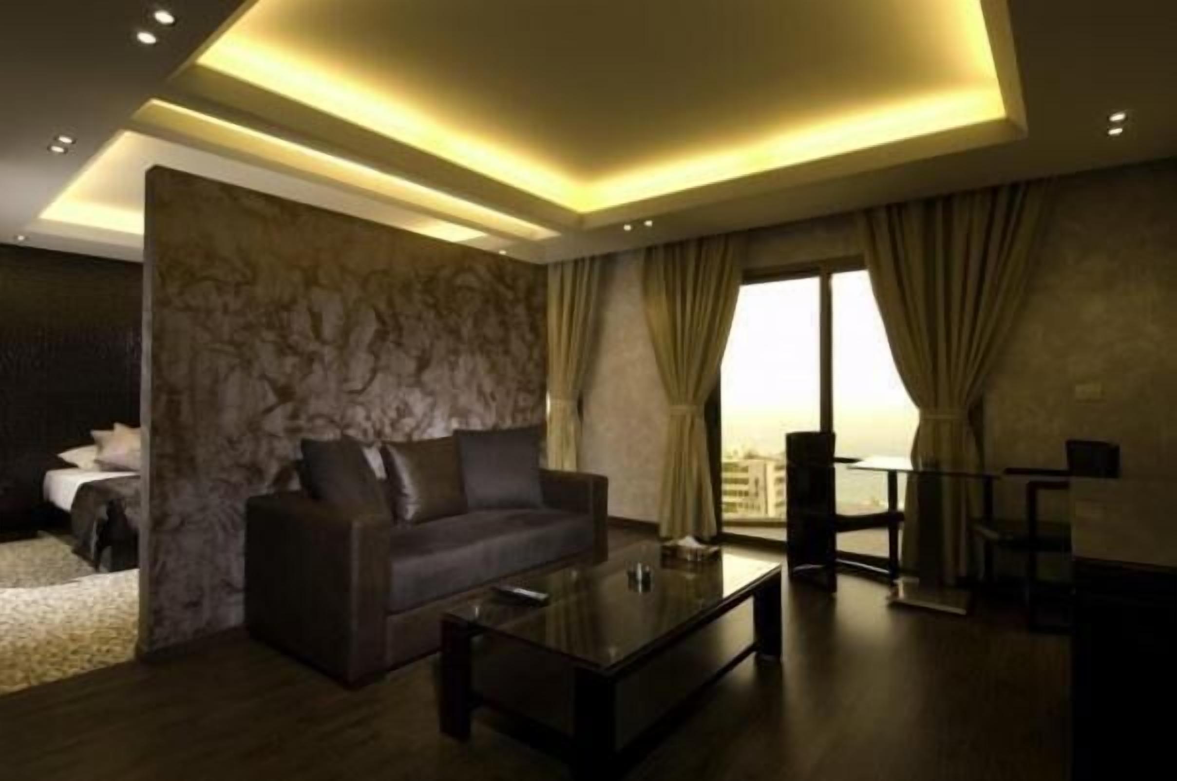 A modern living room with a dark-colored sofa, a glass coffee table, and a view of a cityscape through large windows.
