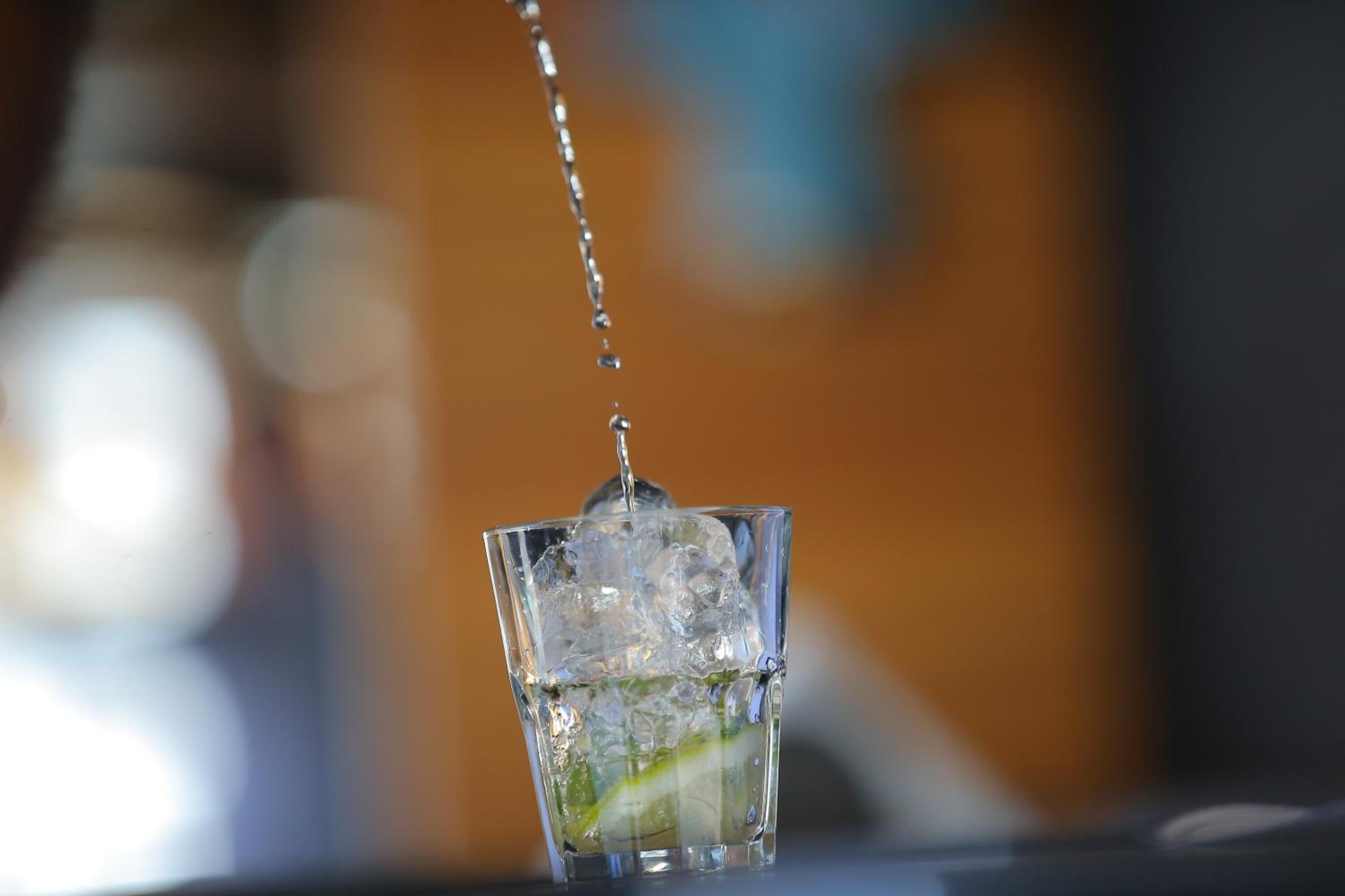A glass with ice cubes and a lime wedge, with water being poured into it.