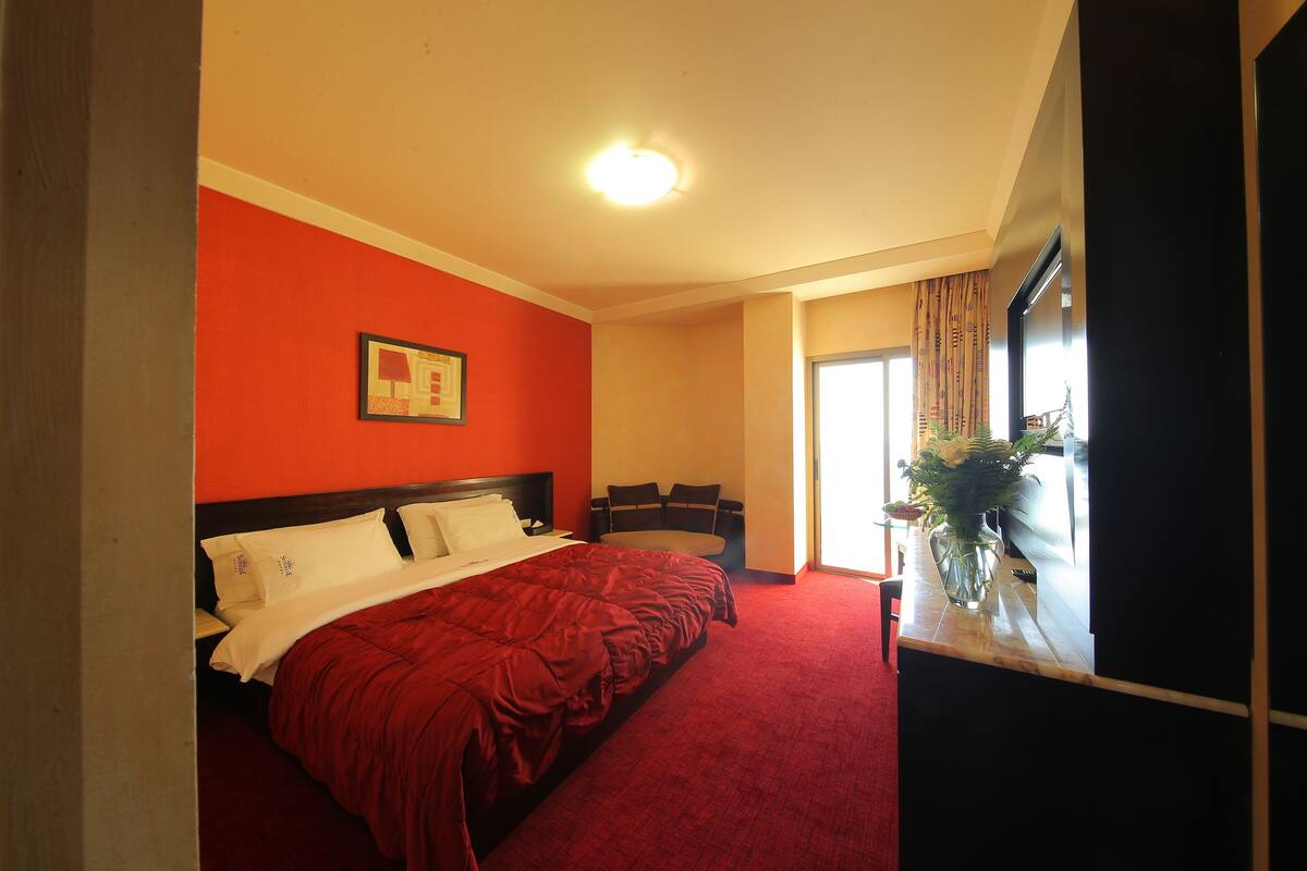 A hotel room with a large bed, a desk with a vase of flowers, and a window with curtains.