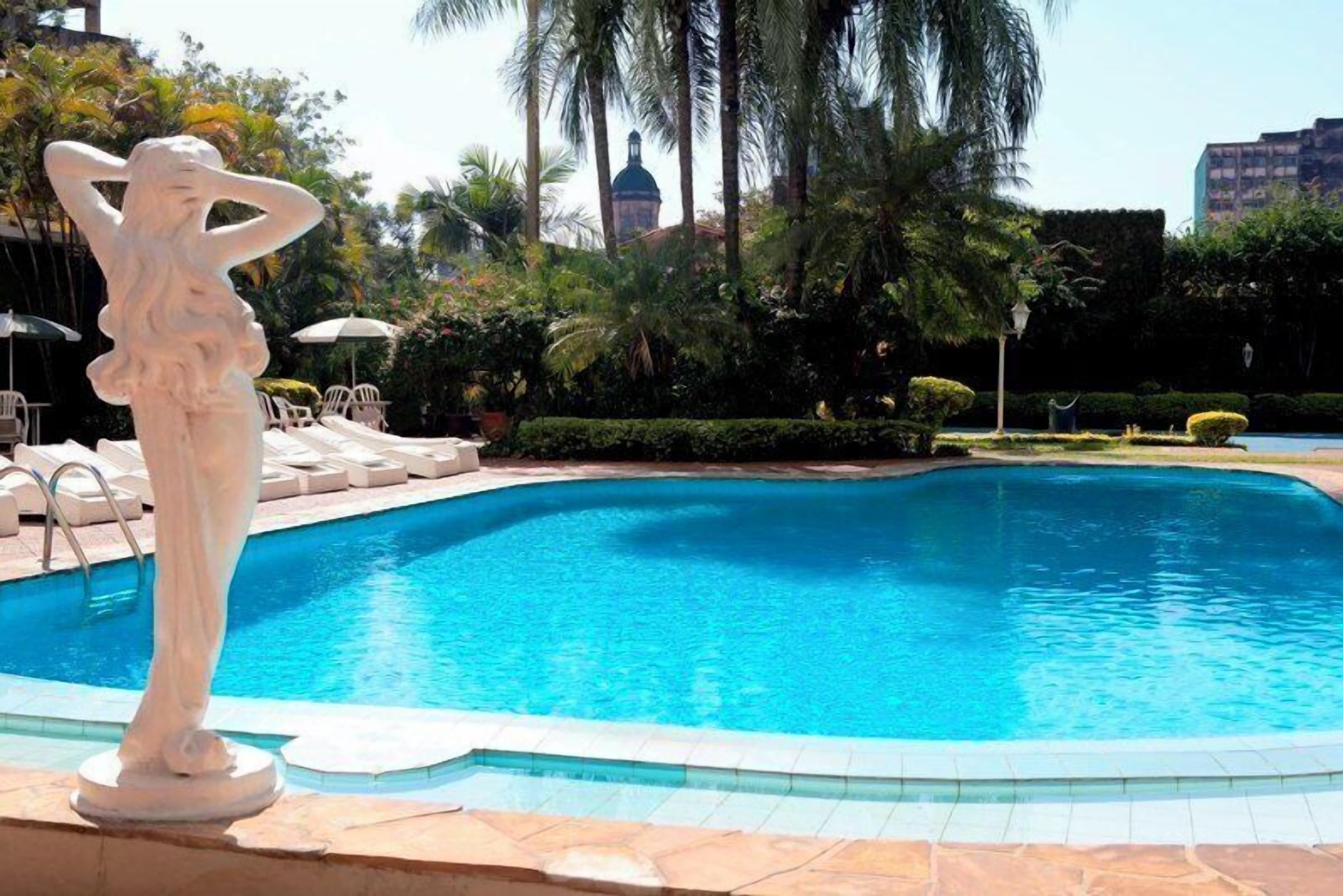 A swimming pool with a statue, surrounded by palm trees and lounge chairs.