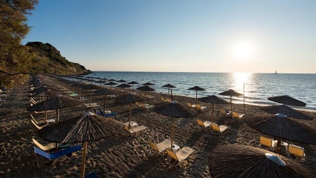 A beach with rows of sun umbrellas and lounge chairs, a clear sky, and the ocean in the background. - Zante Imperial Beach Hotel (Zakynthos)
