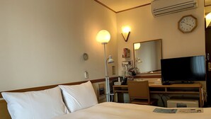 Una habitación de hotel con cama, escritorio, silla, televisor, reloj y lámpara de pared.
