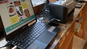 Una computadora portátil sobre una encimera, con un recibo, un teléfono y un ratón.