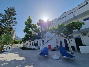 A hotel courtyard with a reception area, a staircase, and lounge chairs. - Leonidas Studios & Apartments (Apokoronas)
