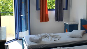 Una habitación de hotel con dos camas, una mesita, una silla, un ventanal con cortinas y un aire acondicionado.
