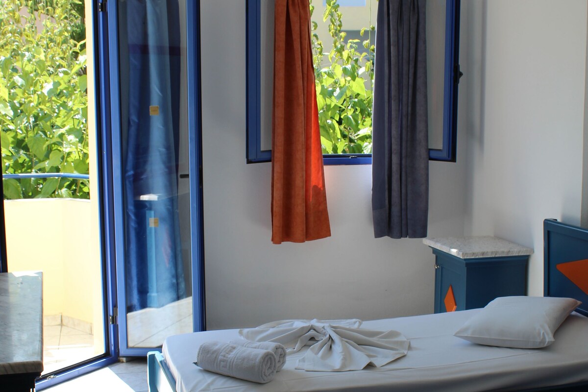 Una habitación de hotel con dos camas, una mesita, una silla, un ventanal con cortinas y un aire acondicionado.