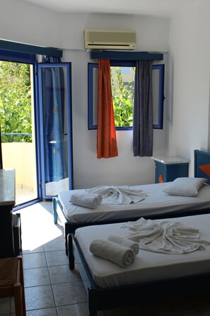Una habitación de hotel con dos camas, una mesita, una silla, un ventanal con cortinas y un aire acondicionado.