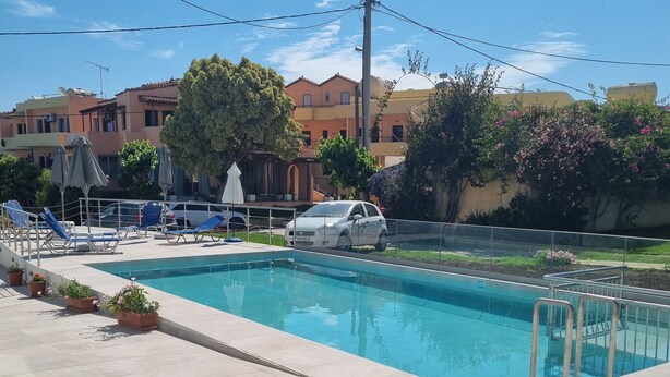 Una piscina con sillones de descanso y plantas en macetas, rodeada de edificios y un coche estacionado.