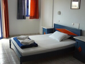 A single bed with a blue and orange headboard, white bedding, and folded towels on the side. - Leonidas Studios & Apartments (Apokoronas)